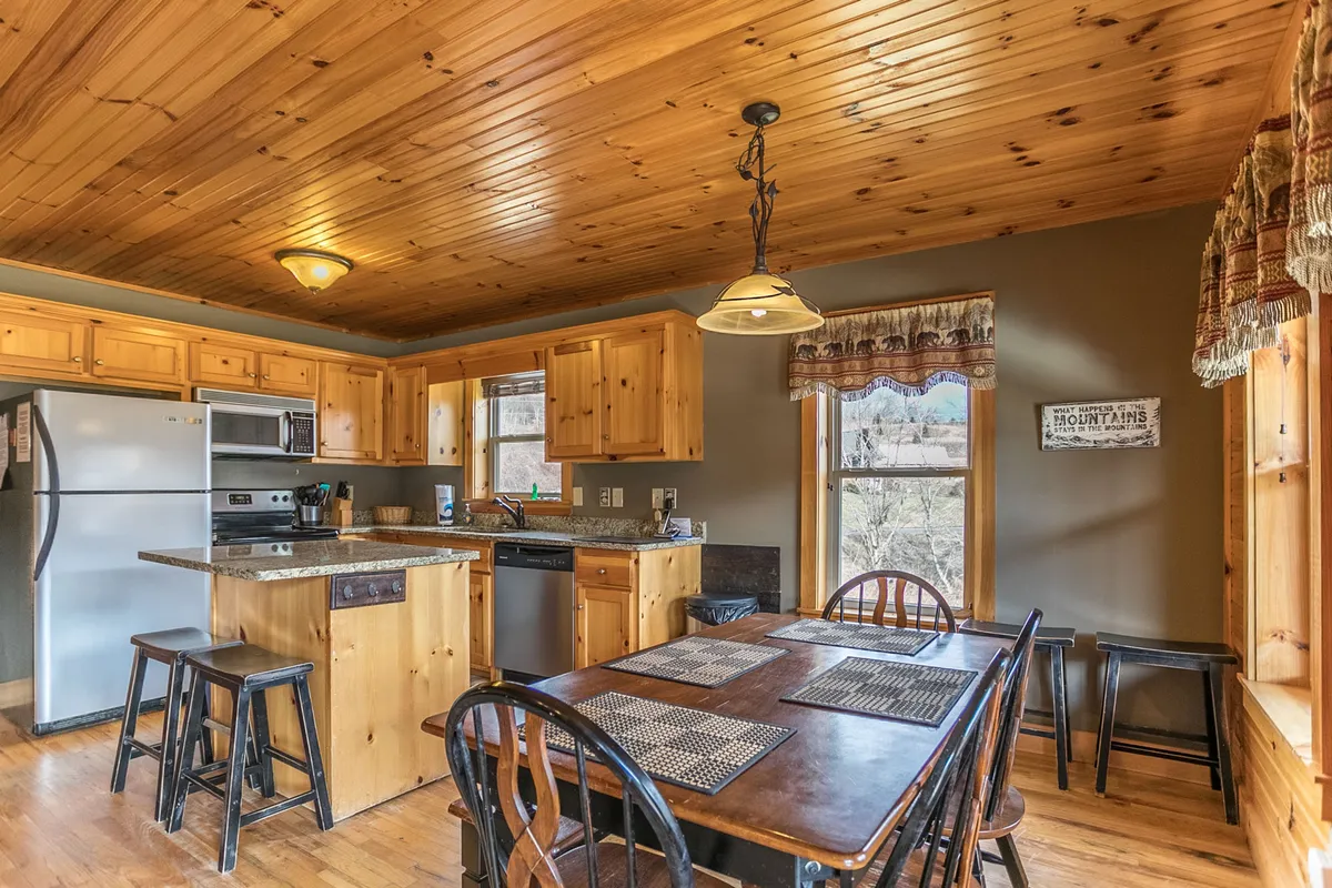 This photo spotlights the gourmet kitchen with wooden cabinetry and granite countertops, the adjacent dining table set for meals, and large windows bringing in natural light. There's a sense of festivity and togetherness, ideal for cooking, celebrating, or casual brunches.