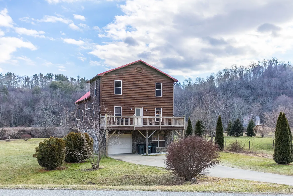 A welcoming view of the cabin’s exterior, showcasing its wooden siding, striking red roof, and inviting front porch with railings. The landscaped yard and porch suggest spaces for outdoor gatherings and relaxation, with natural surroundings hinting at adventure and seasonal enjoyment.