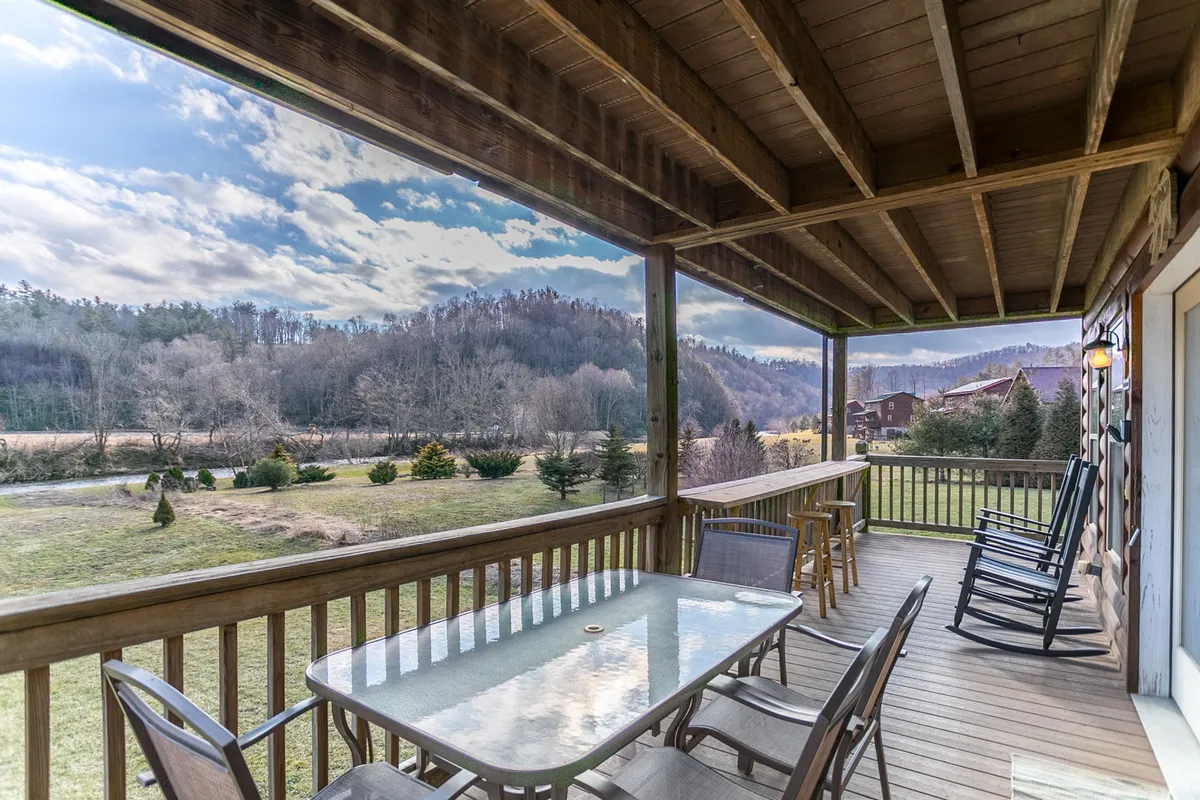 A spacious porch featuring rocking chairs and a dining table set against a gorgeous mountain backdrop. The area invites guests to relax, socialize, or enjoy outdoor meals with mountain views.