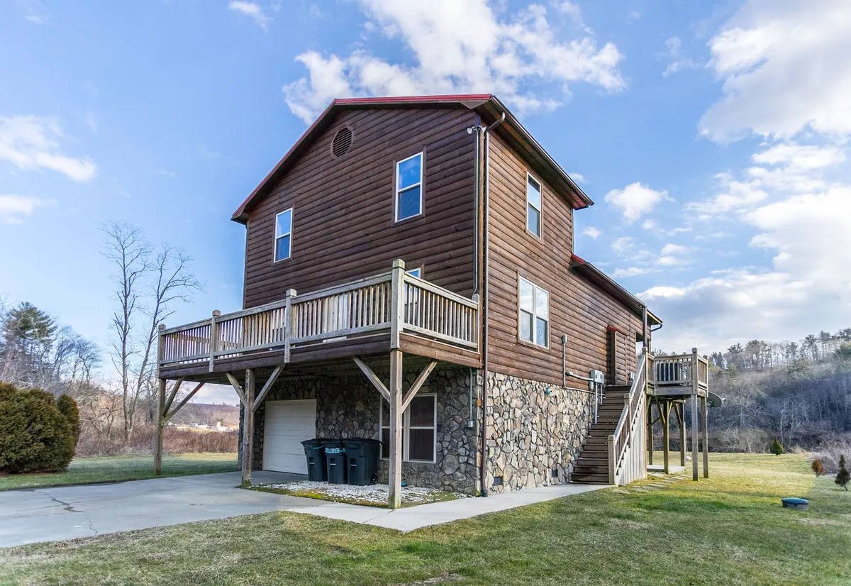 A welcoming exterior view of the wooden deck, stone foundation, large windows, and a green lawn, set up for outdoor gatherings, barbecues, and family activities. The image suggests easy access to nature right from the home.