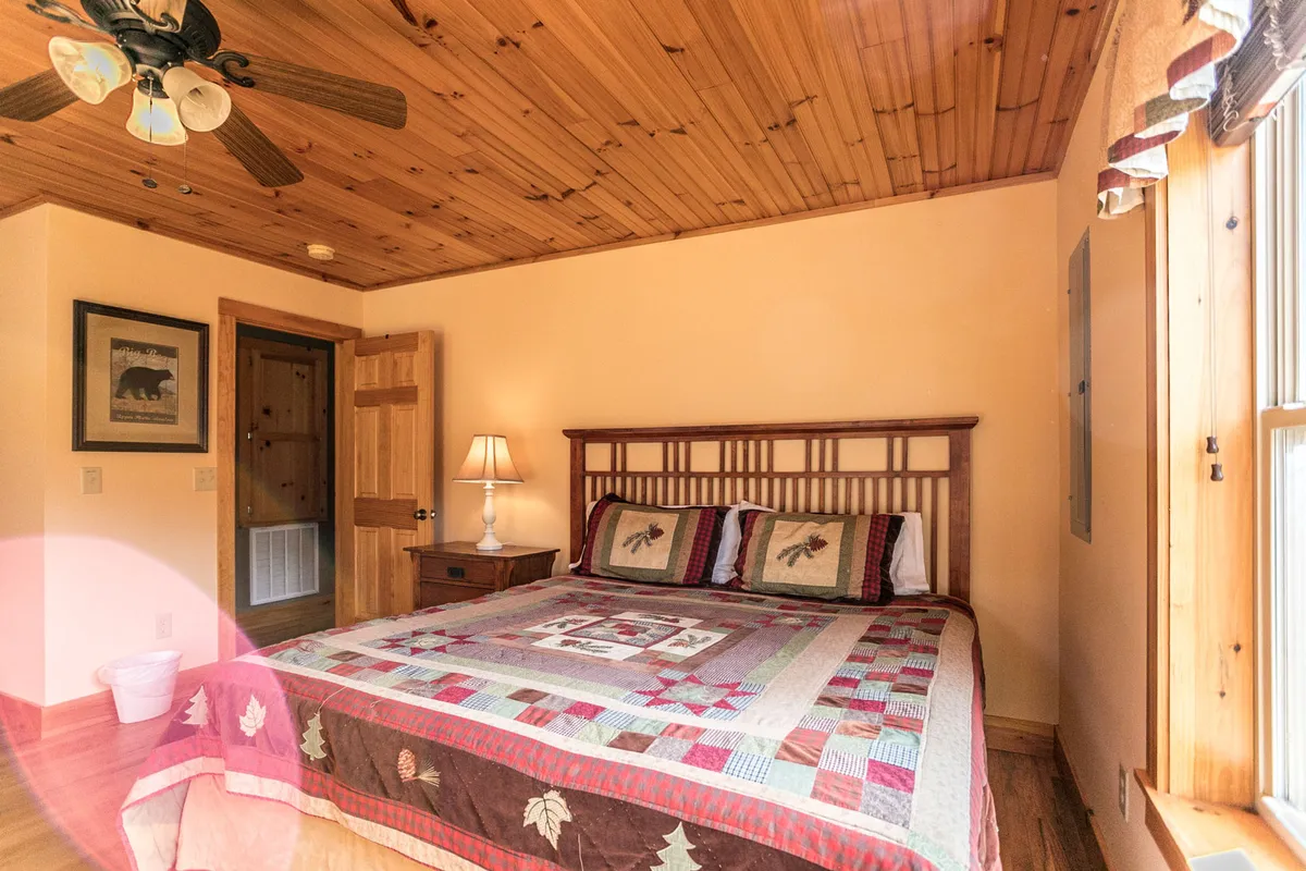A restful bedroom with a soft quilt, lamp, and a framed bear picture above the bed. The wooden door and decor add to the rustic, cabin-like charm, inviting snuggling and shared quiet moments.