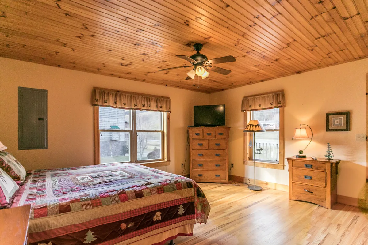 A sunlit bedroom showcasing a bed with a decorative quilt, wooden furniture, and windows that flood the space with natural light, creating a peaceful and welcoming ambiance.