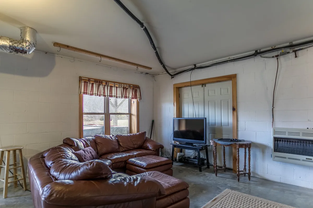 A large, inviting living area with a leather sectional sofa, a TV, and a window with curtains. The cozy setup is perfect for group movie nights, casual conversations, and relaxing together after a day of riverside activities.