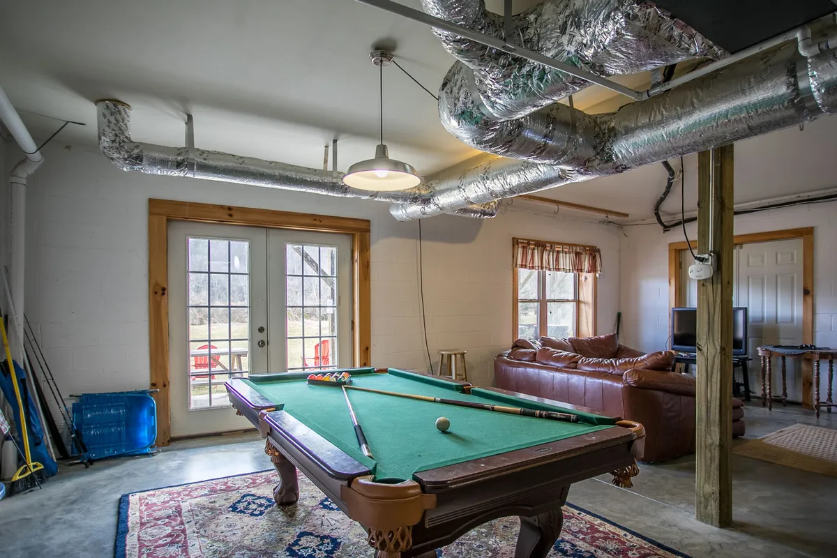 This image showcases a spacious game room featuring a pool table, a comfortable couch, and double doors that lead outside. The setup is ideal for socializing, hosting friendly competitions, and provides a visual connection between indoor activities and outdoor access.